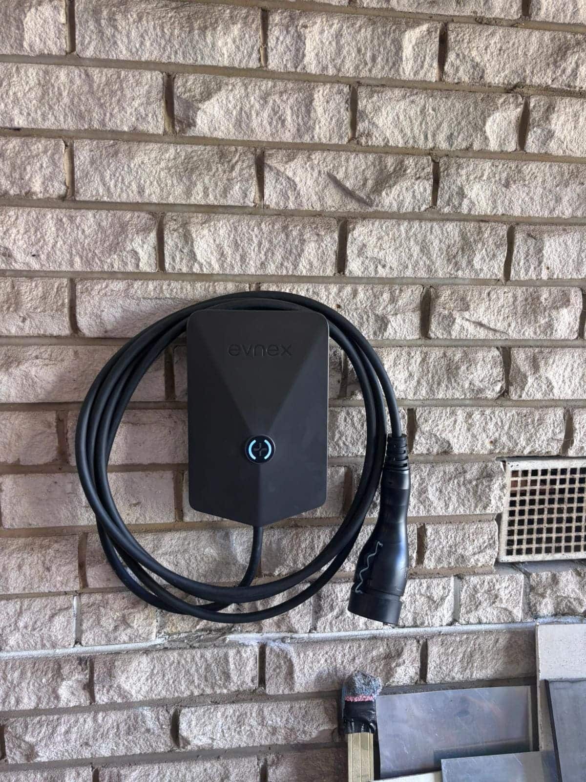 Evnex electric vehicle charging station mounted on a brick wall outdoors.