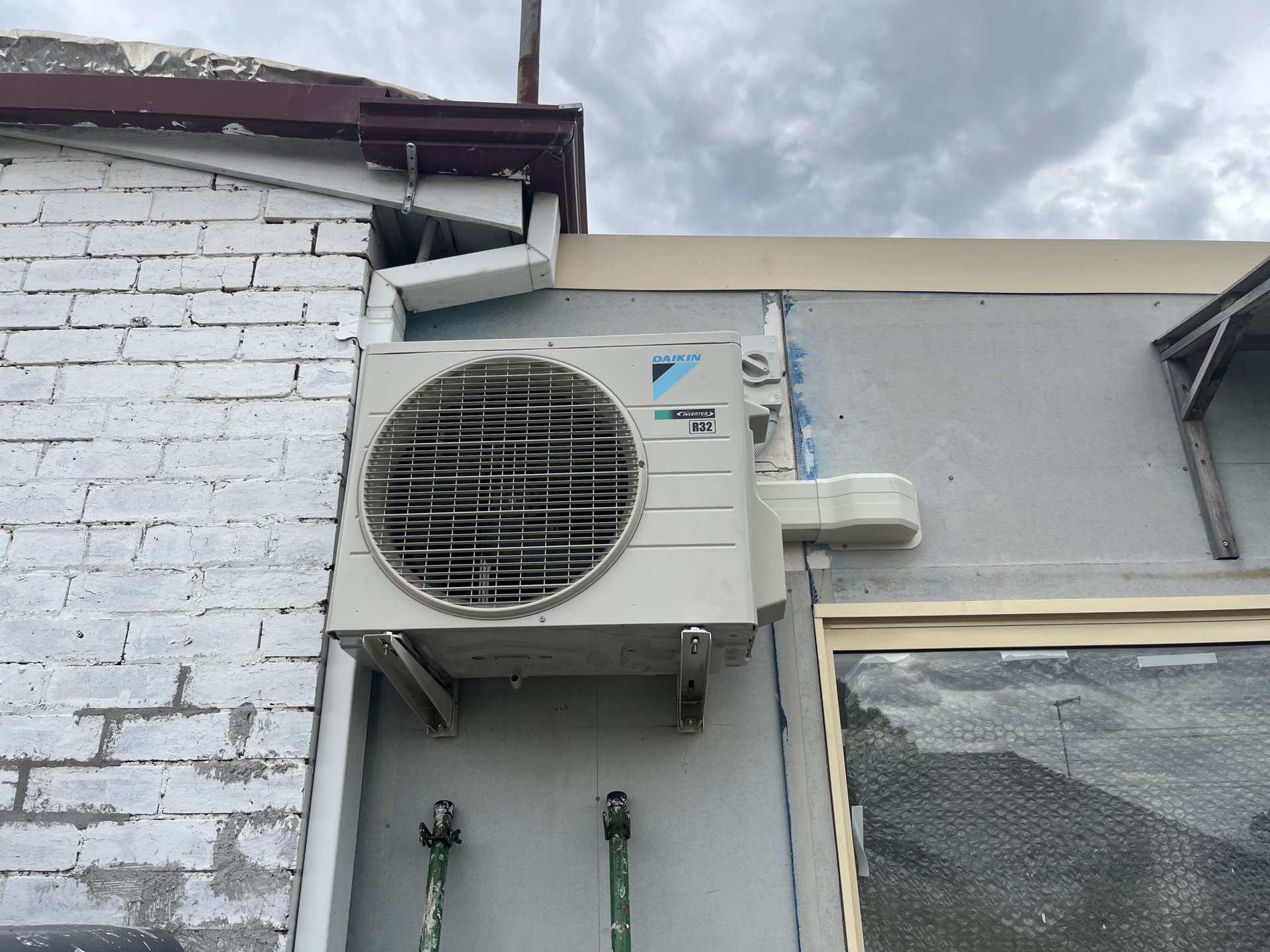 Air conditioning unit mounted on exterior wall of building, outdoors on a flat surface under cloudy sky.