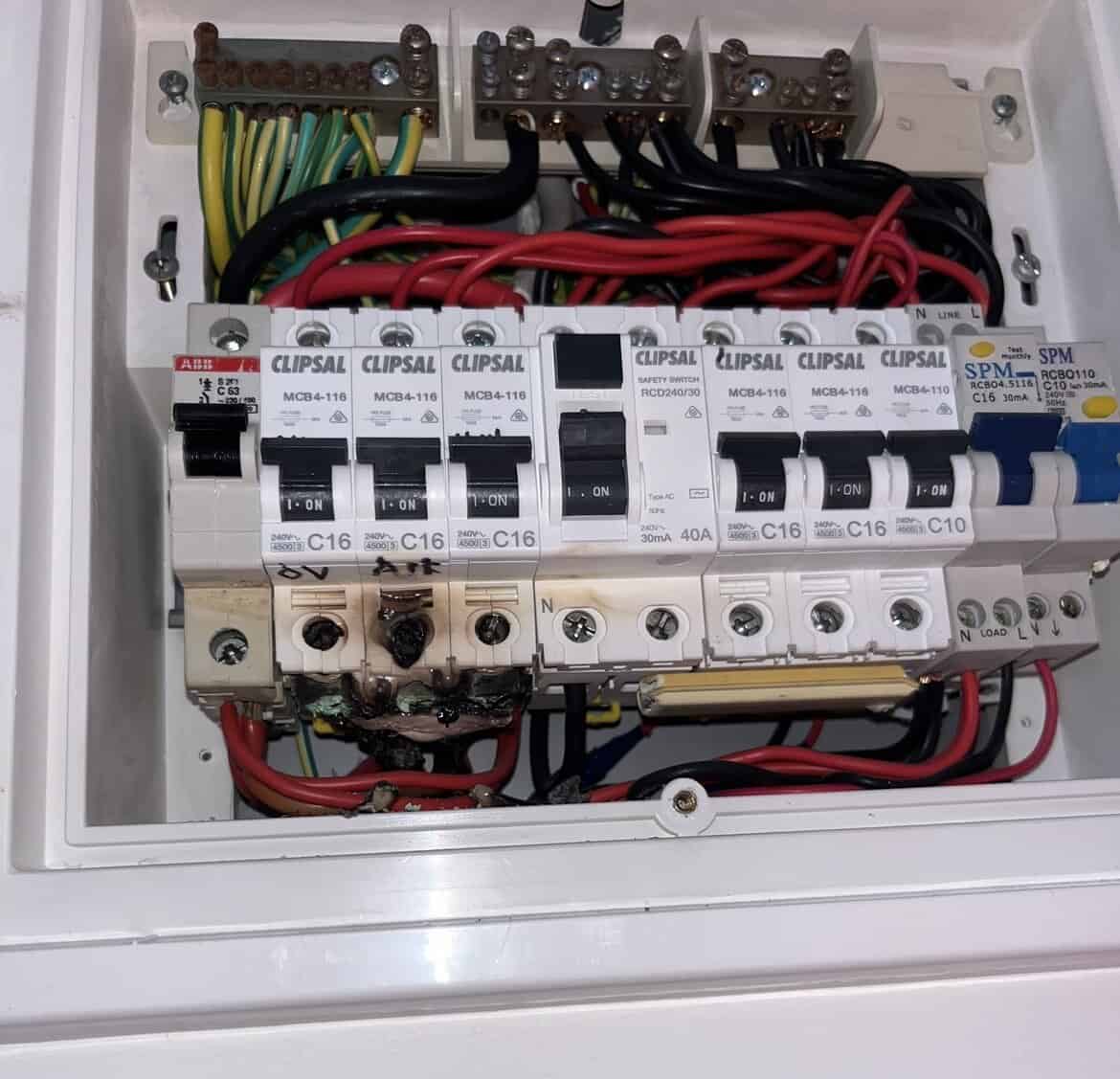 - Thin metal electrical switchboard with circuit breakers, mounted inside a white electrical enclosure outdoors.