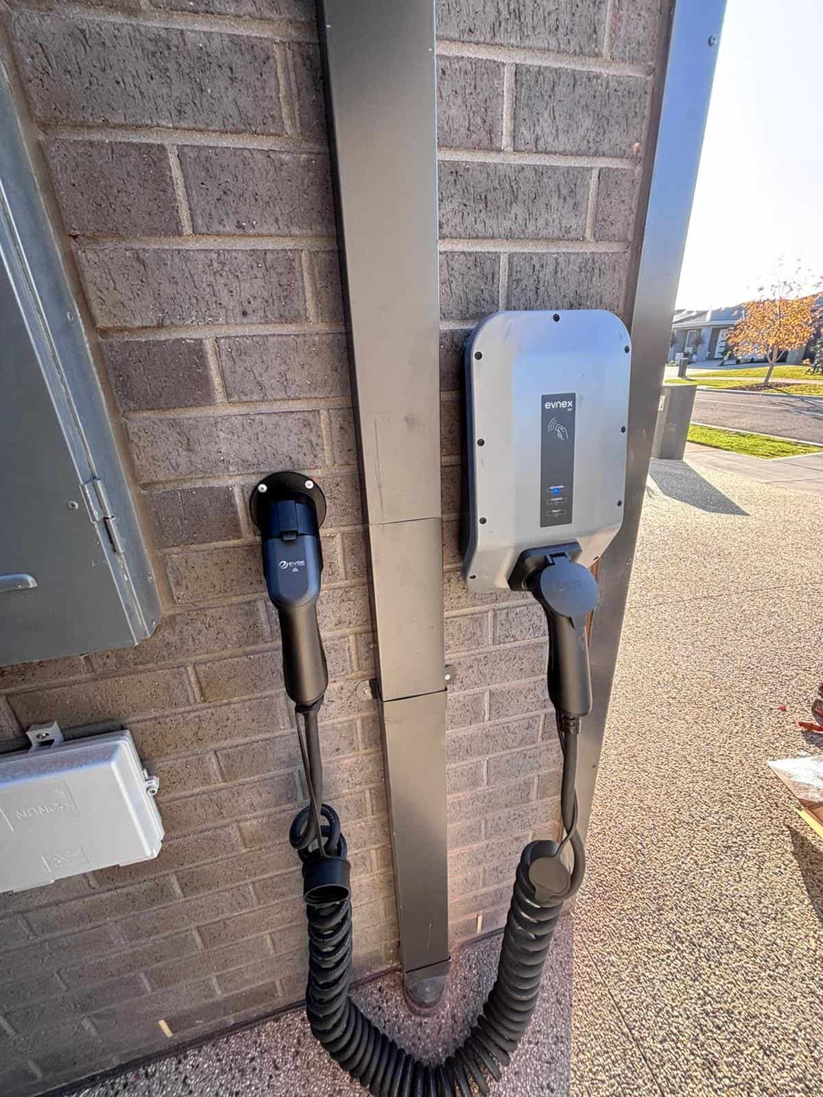 EV charger unit mounted on brick wall outside building, connected to power outlets.