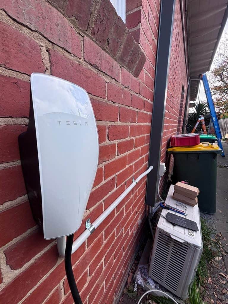 Tesla solar inverter mounted on a red brick exterior wall.