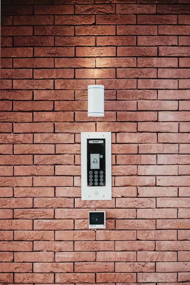 Smart intercom and lighting control system mounted on a red brick wall outside a building.