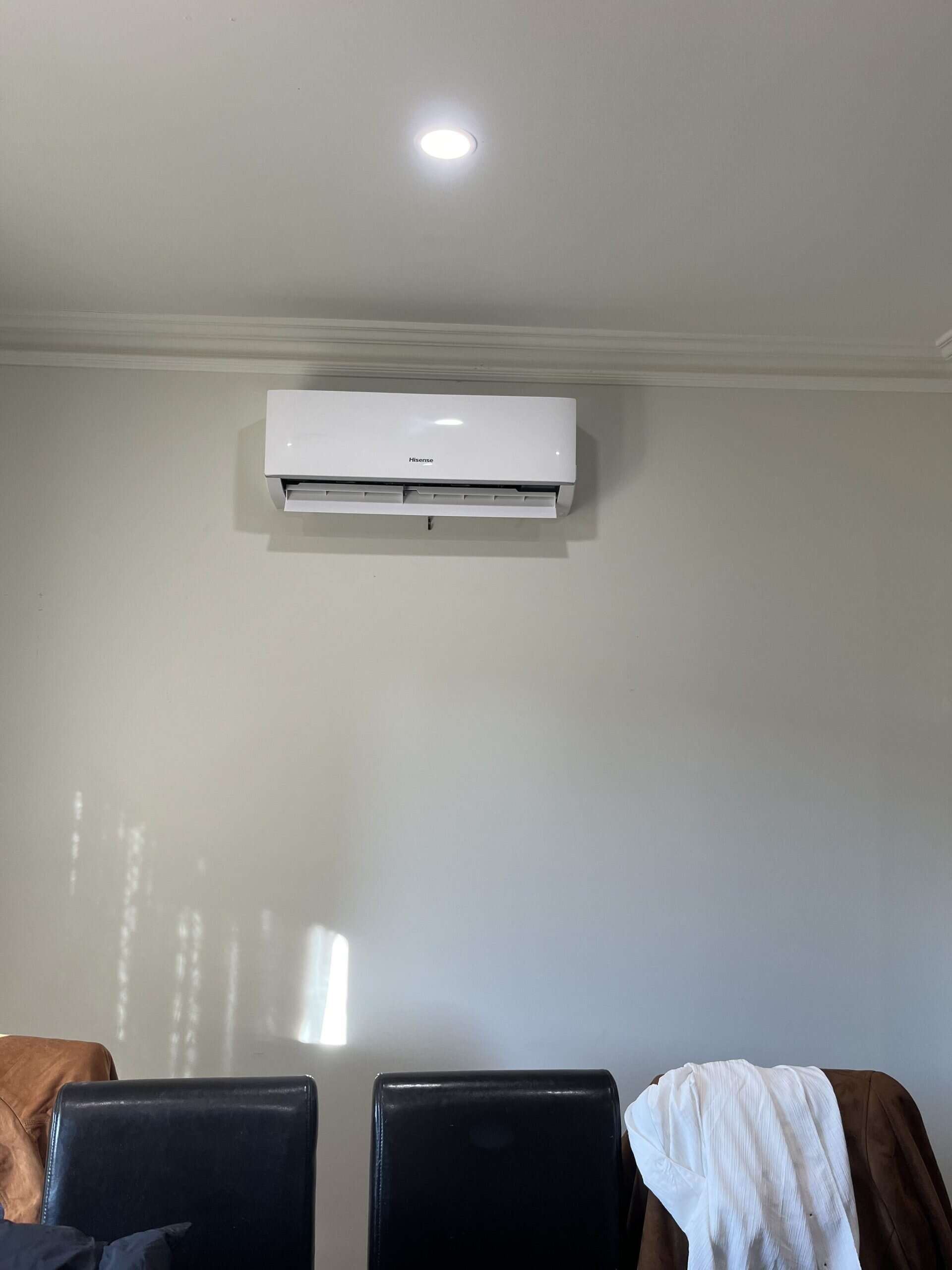 Wireless air conditioning unit installed inside a living room on a smooth wall above dining chairs.