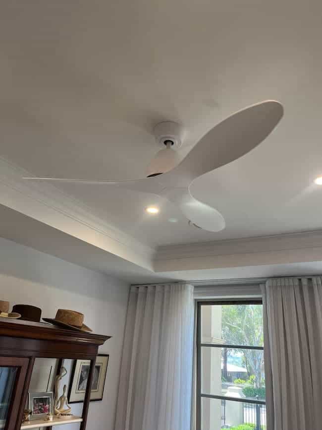 Fan on ceiling in a living room with white walls and curtains, located indoors.