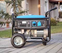 Industrial portable generator on paved driveway outside house, with black handles and large wheels, used for electrical power supply during outages or outdoor jobs.