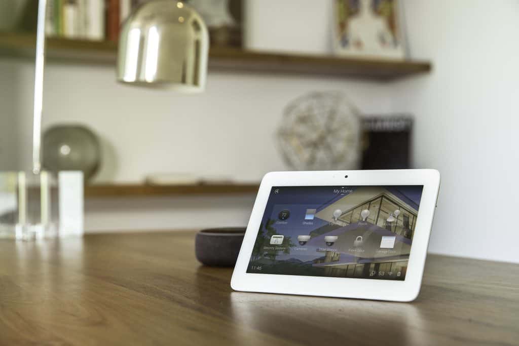 Home automation touchscreen device on a wooden kitchen bench inside a modern home.