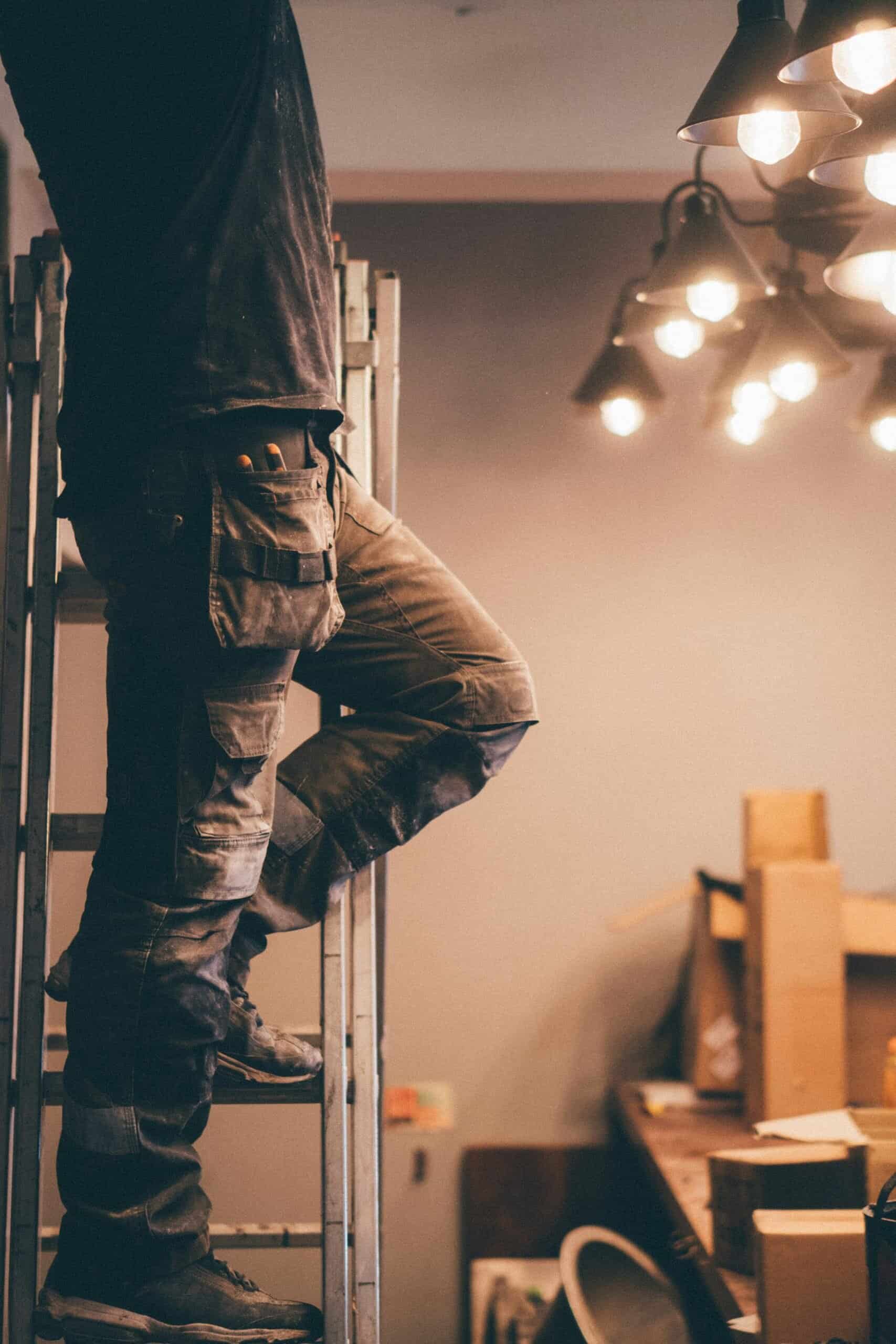 Wiring electrician working indoors on a wooden staircase with tools in pocket.