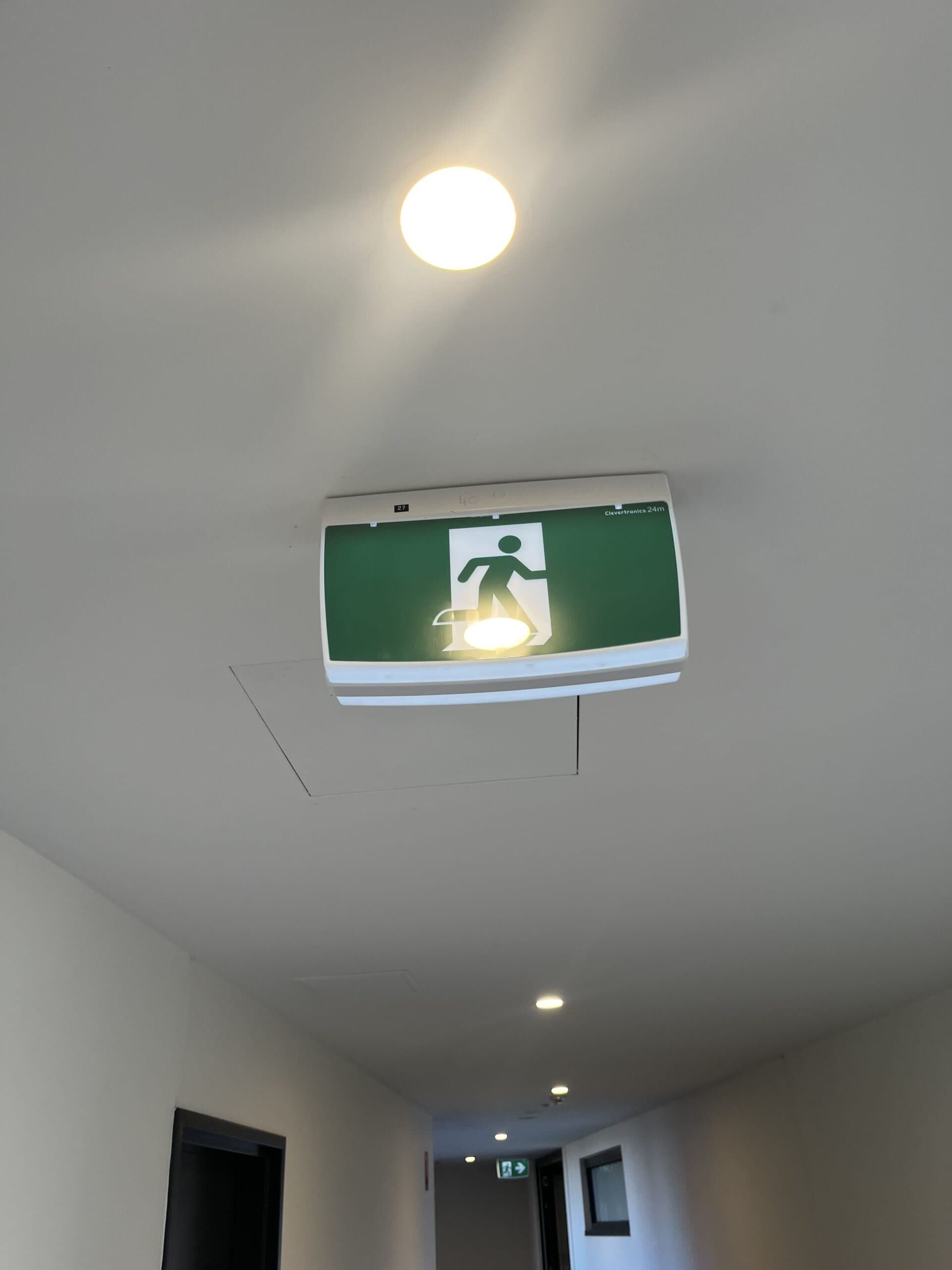 Emergency exit sign illuminated on an indoor ceiling corridor surface.