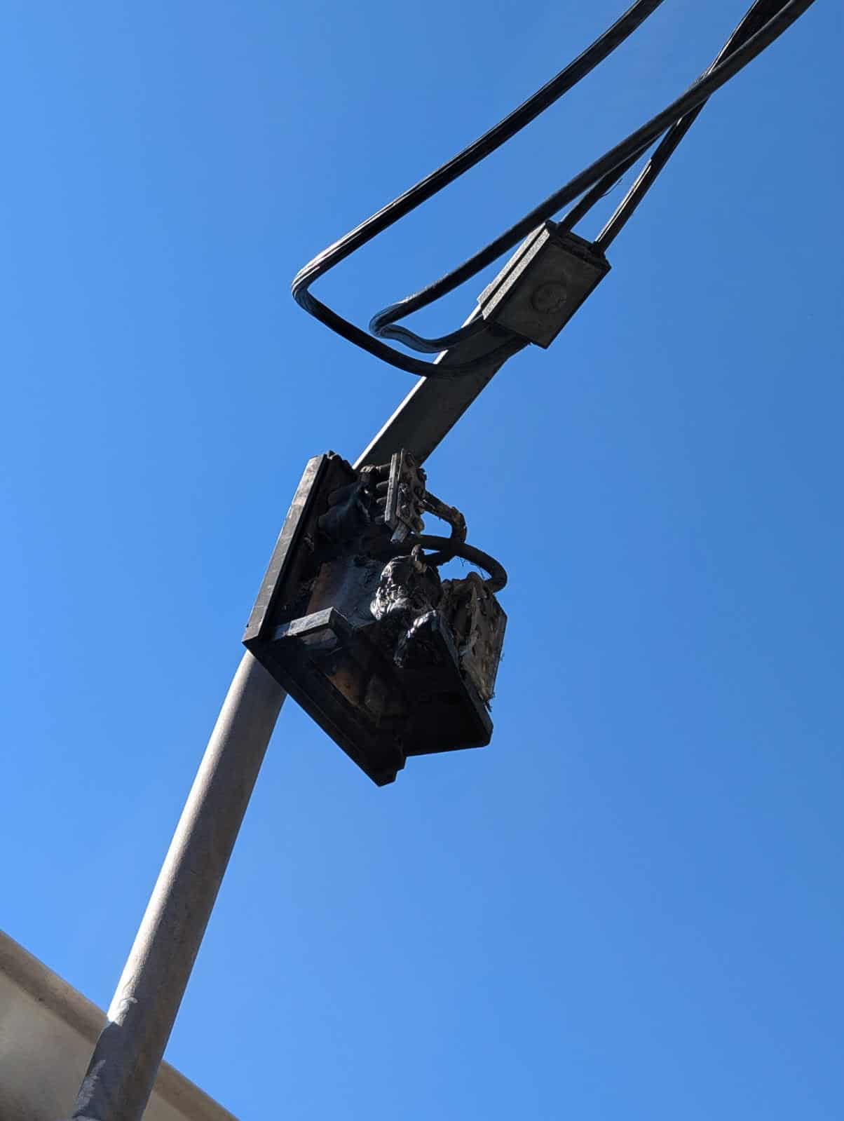 Damaged electrical transformer mounted on a utility pole outside against a clear blue sky.