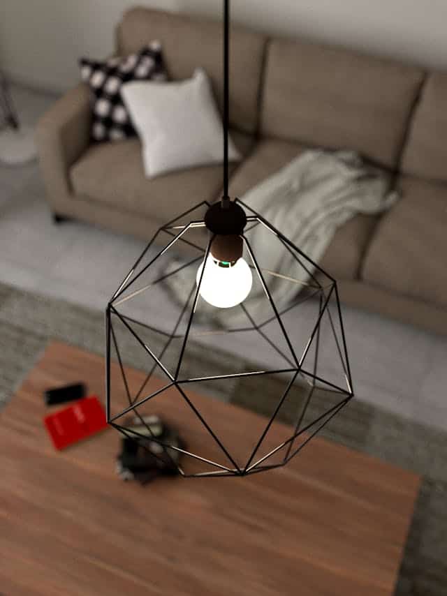 Pendant light fixture with geometric black metal frame hanging inside a living room, illuminating a coffee table and sofa area.