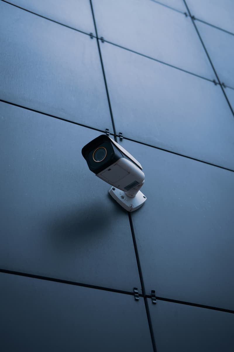Sky security camera mounted on exterior building wall, outside on the grey tiled surface, capturing surveillance footage in an urban environment.