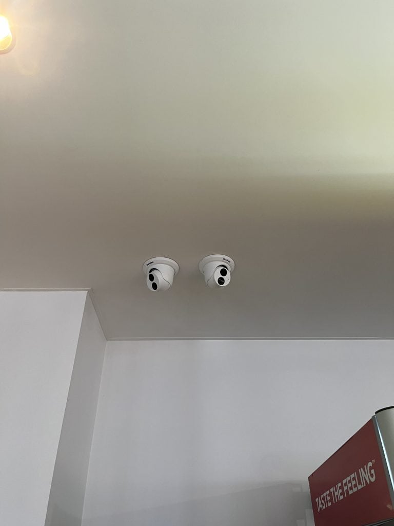 Two white ceiling smoke detectors installed on a smooth ceiling inside a room.
