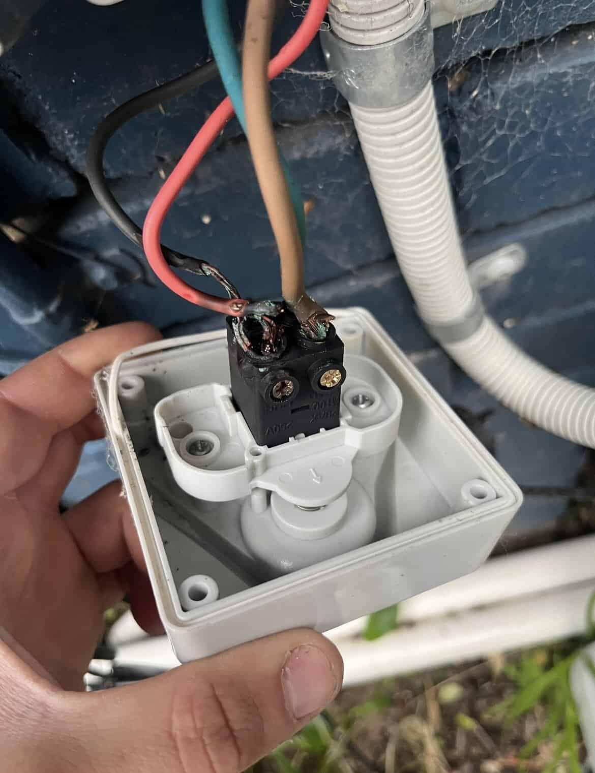 Wiring in an outdoor electrical box mounted on a wall, with electrical wires connected inside.