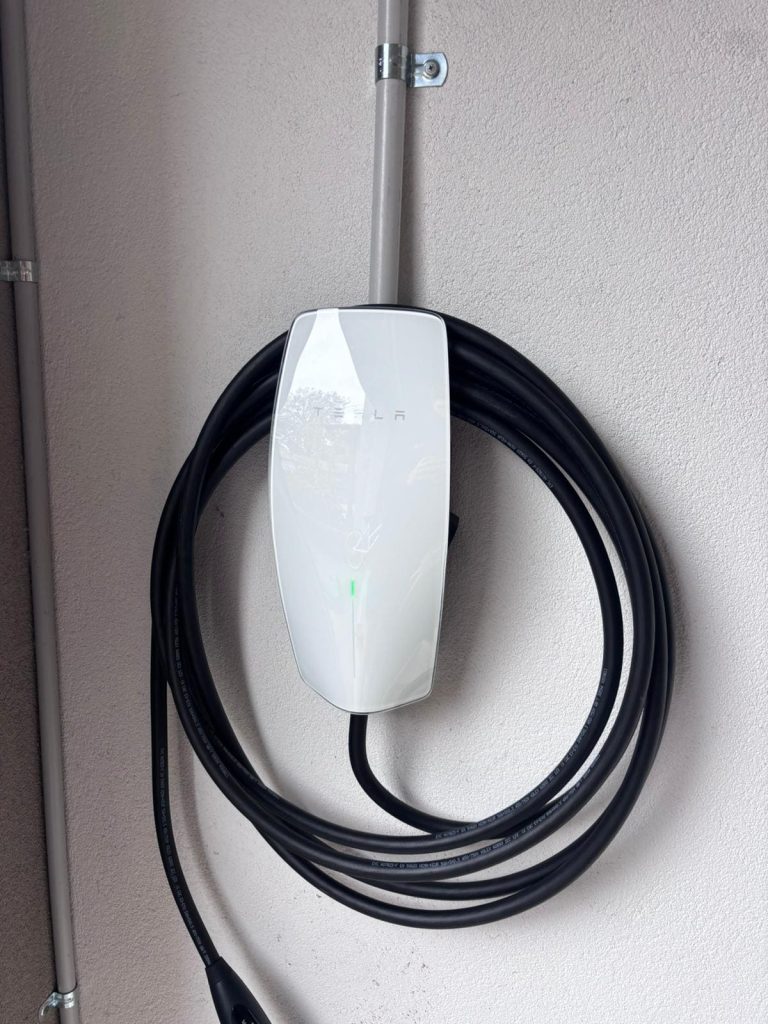 Tesla wall charger mounted on an outdoor wall surface.